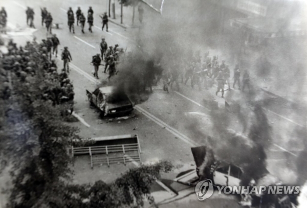 1980년 5월 광주 시가지에서 계엄군으로 출동한 공수부대와 시민들이 충돌, 차량이 불타고 있다. 5월 18일 밤부터 격화된 시위는 5월 21일 전남도청 앞에서 시위대의 차량 돌진, 이를 저지하기 위한 계엄군의 집단발포로 격화되었다.(연합뉴스 제공)