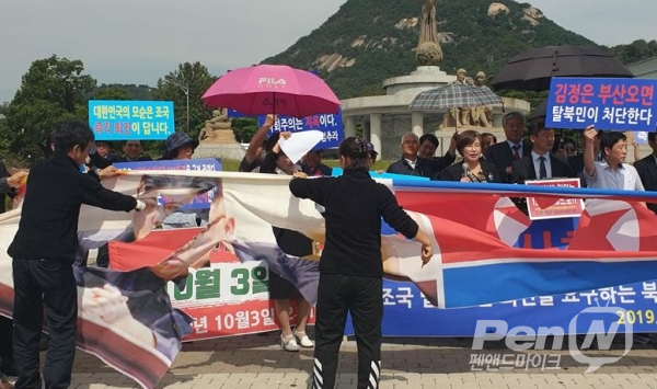 탈북민지식인들이 시국선언에 앞서 김정은과 인공기 천막 사진을 커터칼로 도려내고 있다.