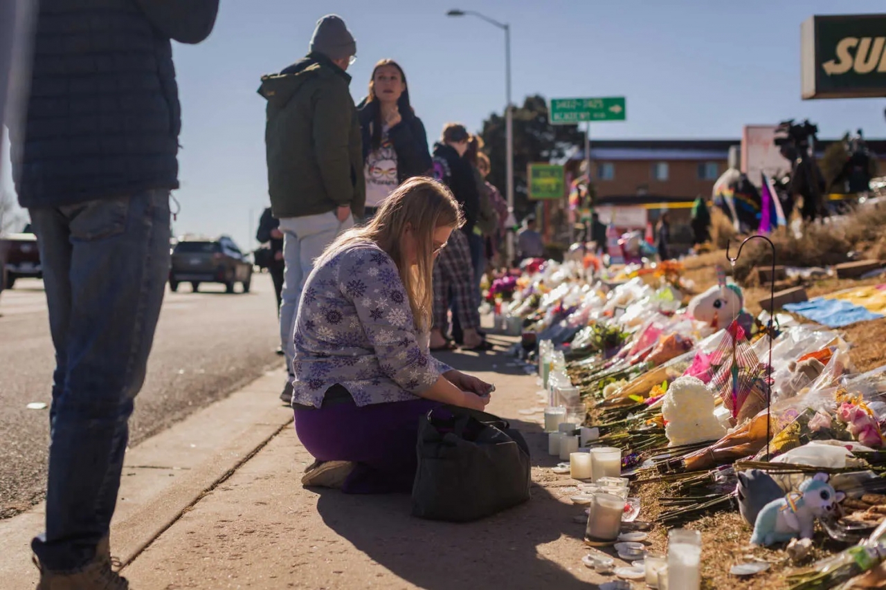 이번 총기난사 사건 사망자들을 추모하는 어느 미국인이 무릎 꿇고 있으며, 헌화된 꽃다발들이 놓여져 있다. [사진=뉴욕타임스]
